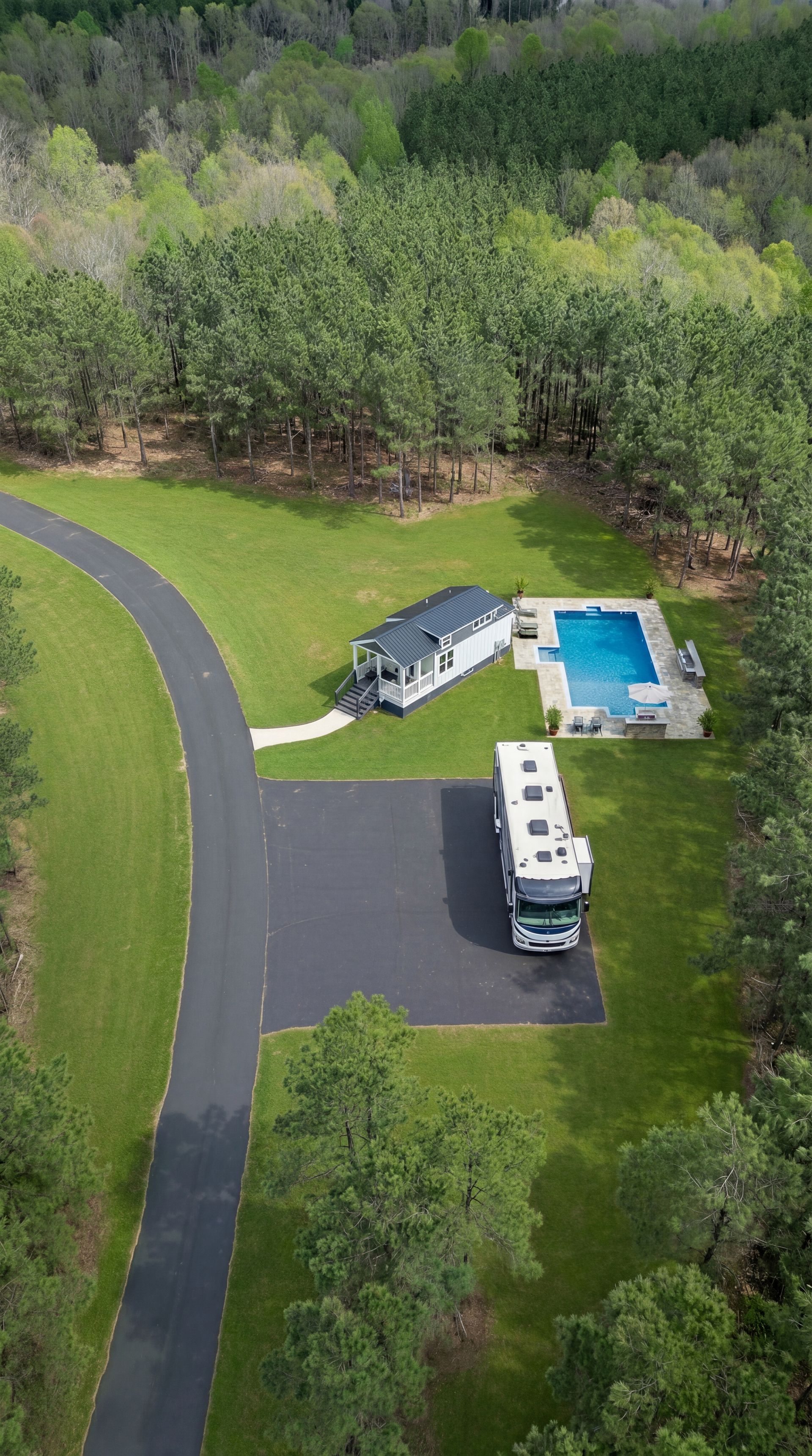 Aerial view of a house with a driveway, RV, and backyard pool beside a wooded area.