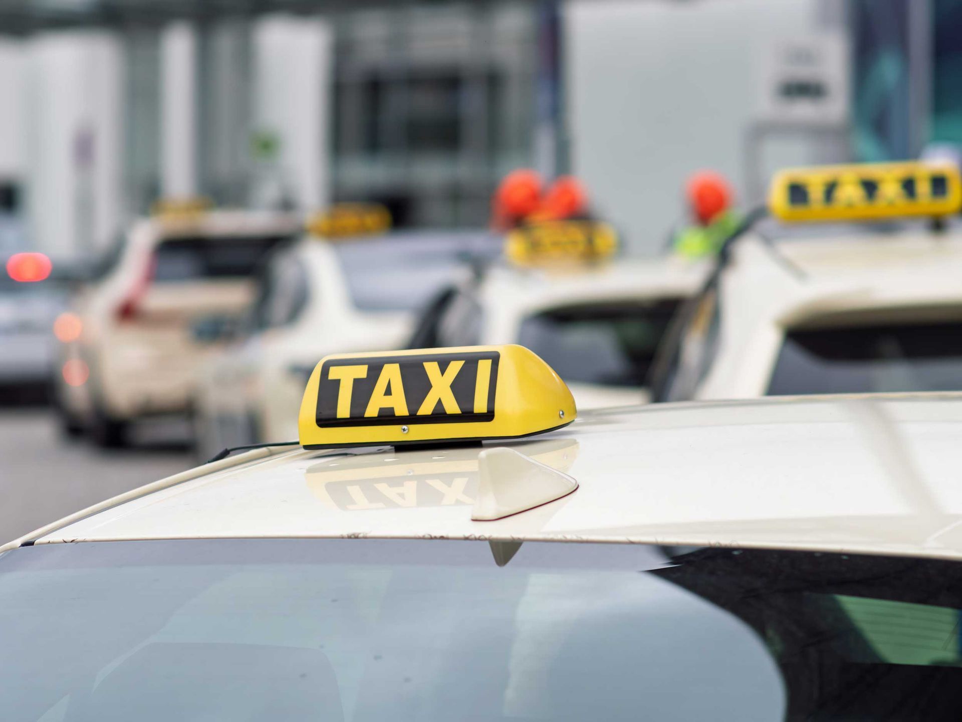 Yellow taxi roof sign on parked taxi cars in city street traffic scene area view background setting.