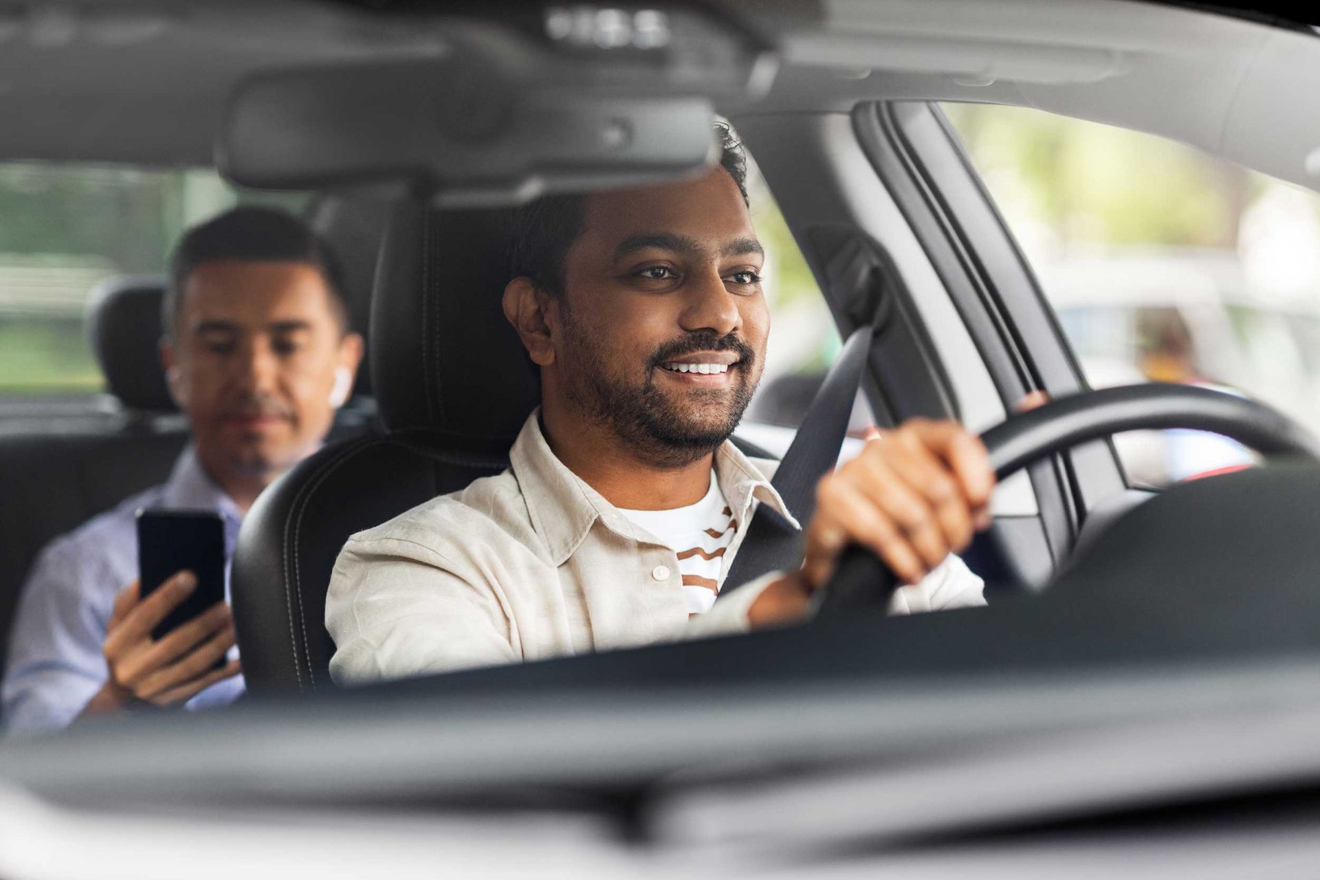 Driver steering a car with a passenger in the back seat using a phone during a taxi ride. Driver steering a car with a passenger in the back seat using a phone during a taxi ride.