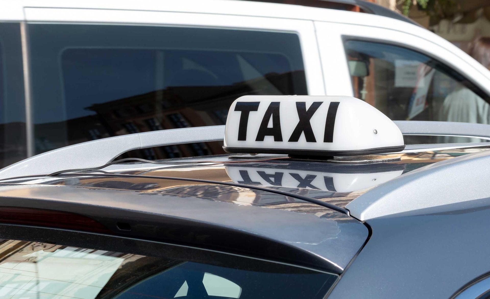 Roof sign with the word “TAXI” mounted on top of a parked cab. Roof sign with the word “TAXI” mounted on top of a parked cab.