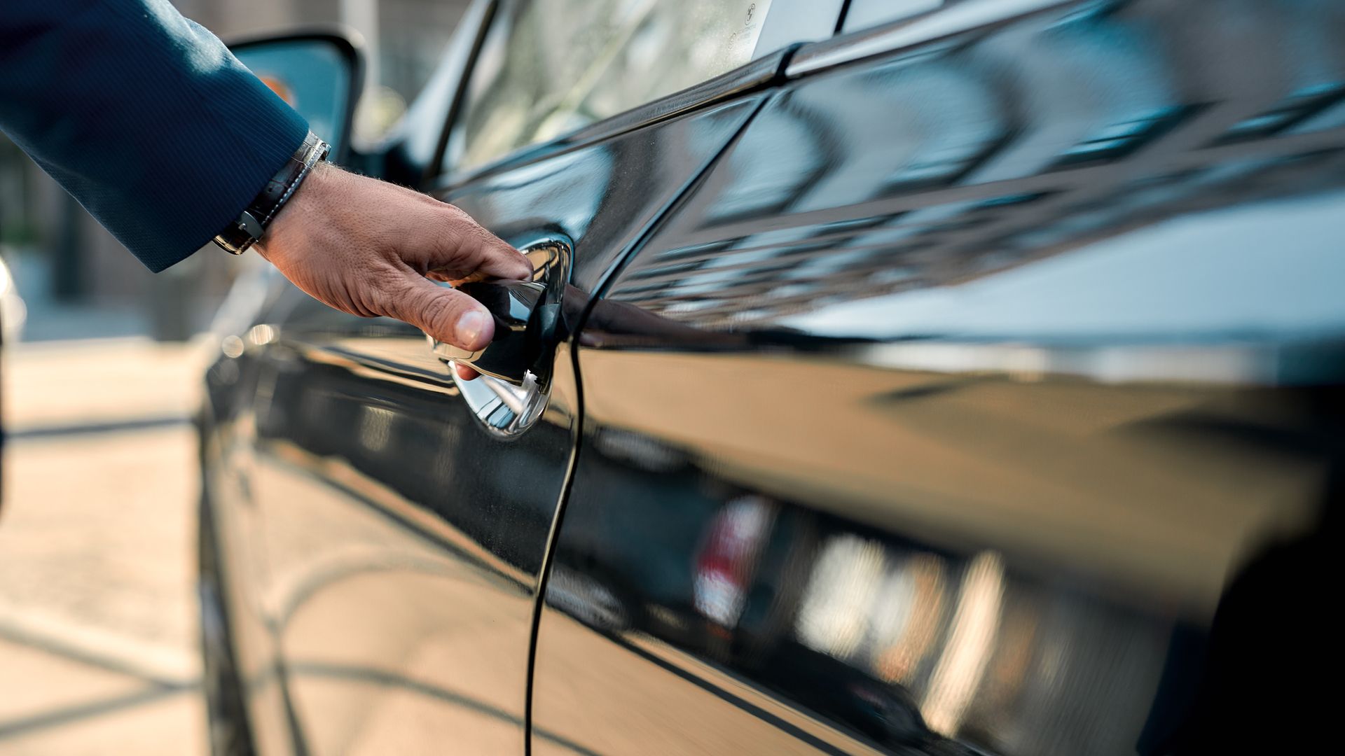 Cropped photo of a male hand opening the door of a black limousine while standing outdoors.