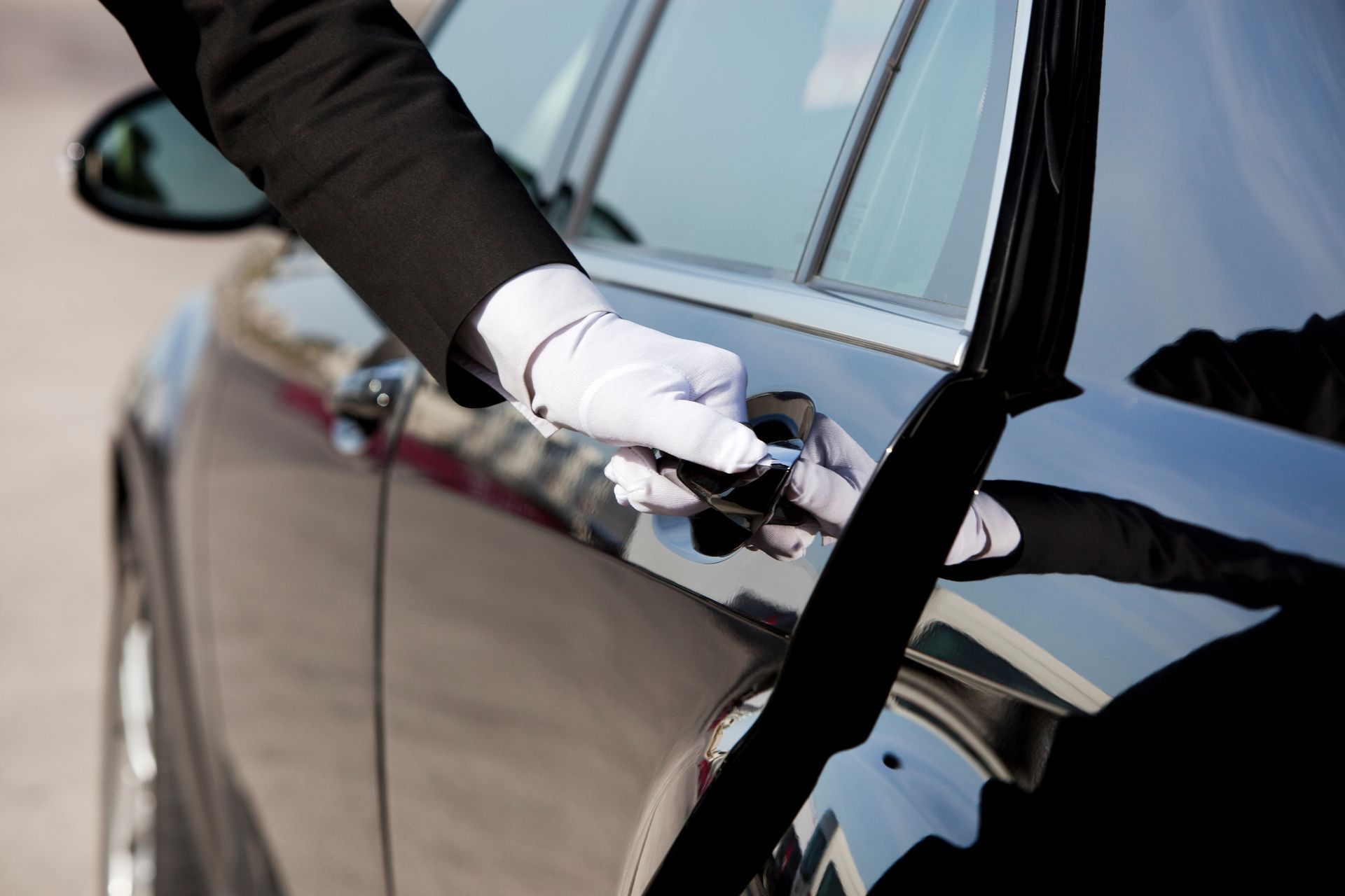 A man in a tuxedo is opening the door of a car
