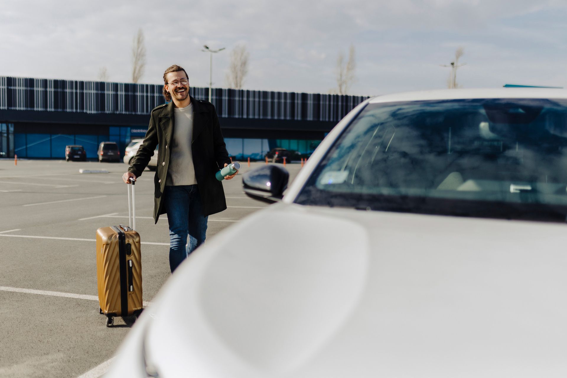 A smiling man with a yellow suitcase is going to his taxi, showcasing airport taxi service.