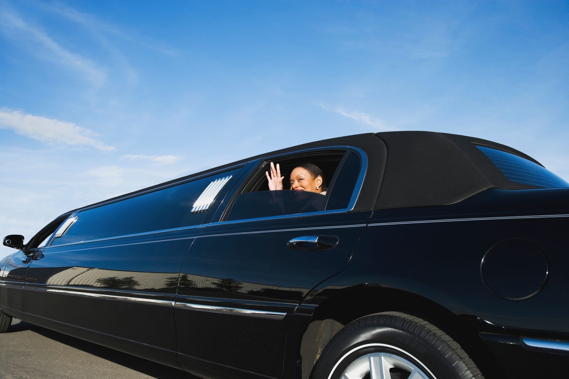 A woman in a limousine waving, representing elegance & the joy of limousine transportation service.