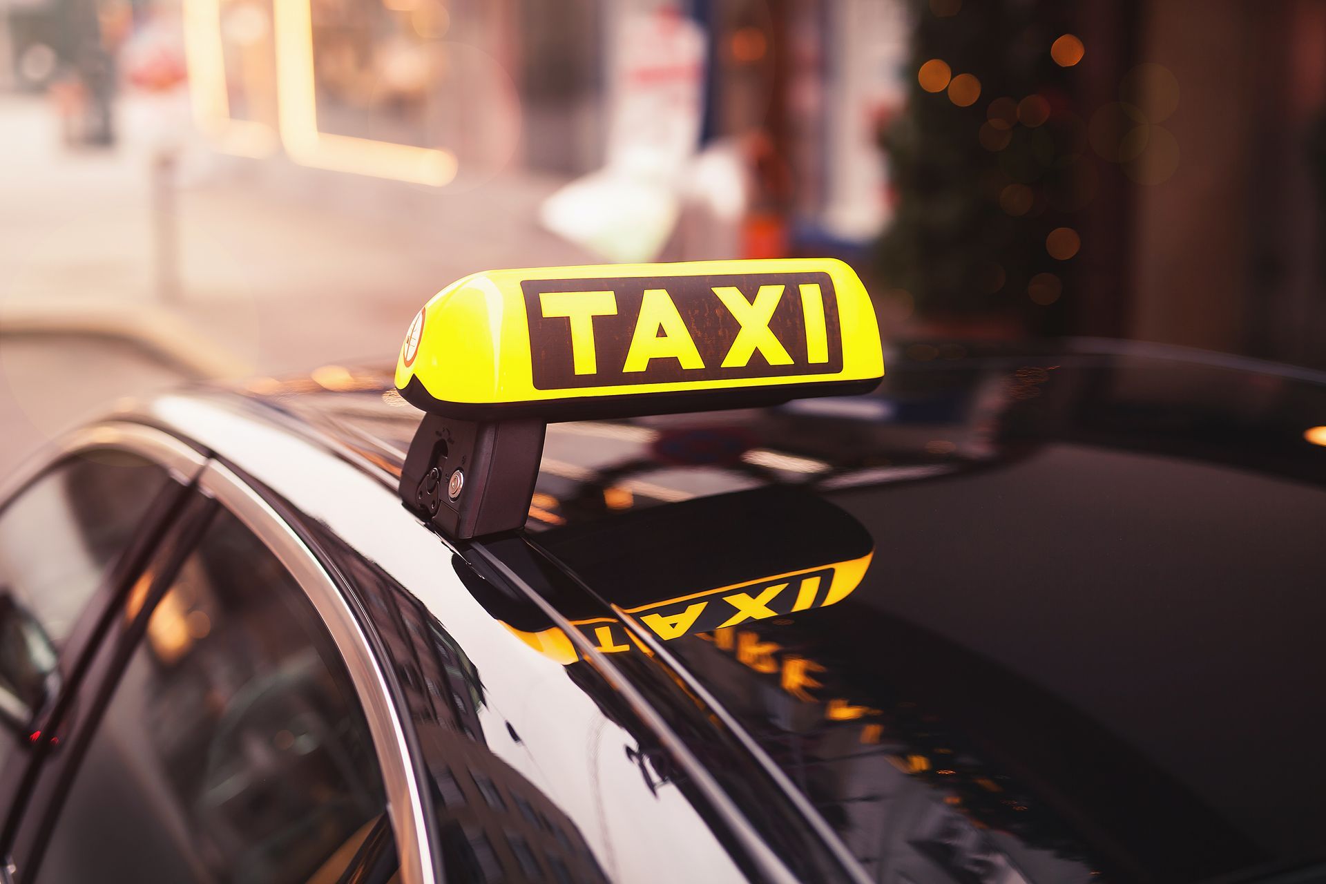 A black car with a yellow taxi sign on the roof.