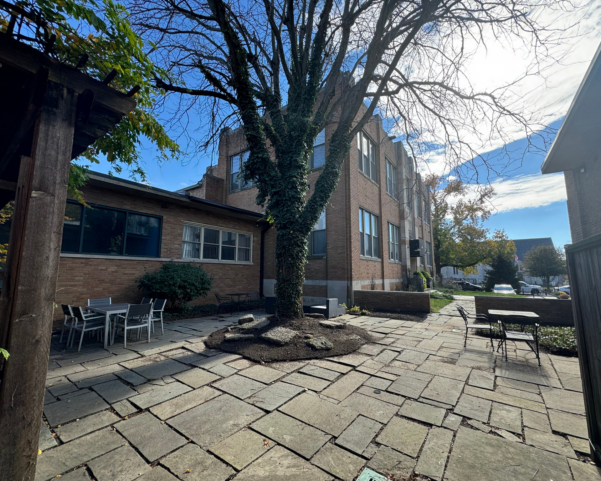 A stone patio with tables and chairs in front of a brick building.
