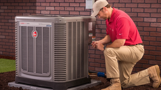 A man is sitting on the floor fixing an air conditioner.