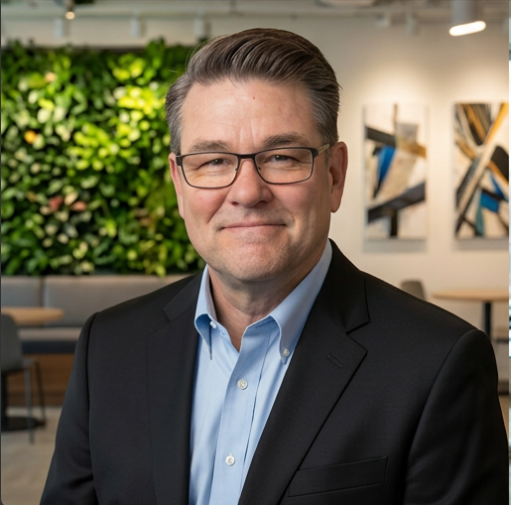 Man in glasses and suit smiling, standing in front of green wall and abstract art.