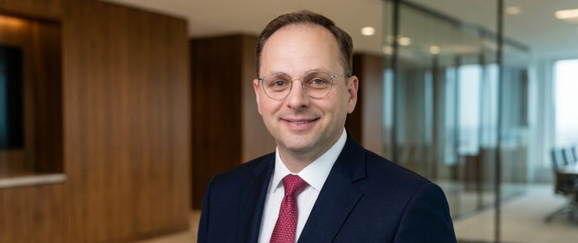 Man in suit and glasses smiling, office background.