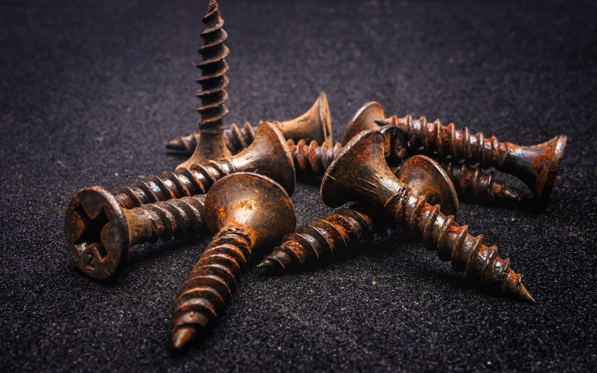 A pile of rusty screws on a black surface.