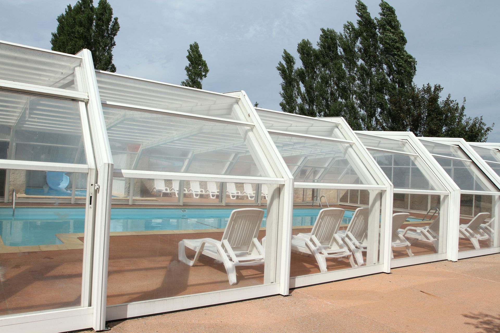 A swimming pool with a clear roof and chairs underneath it
