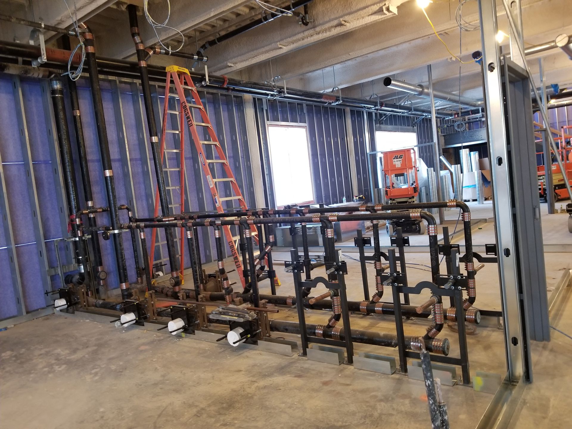 A room with a lot of pipes and a ladder in it.