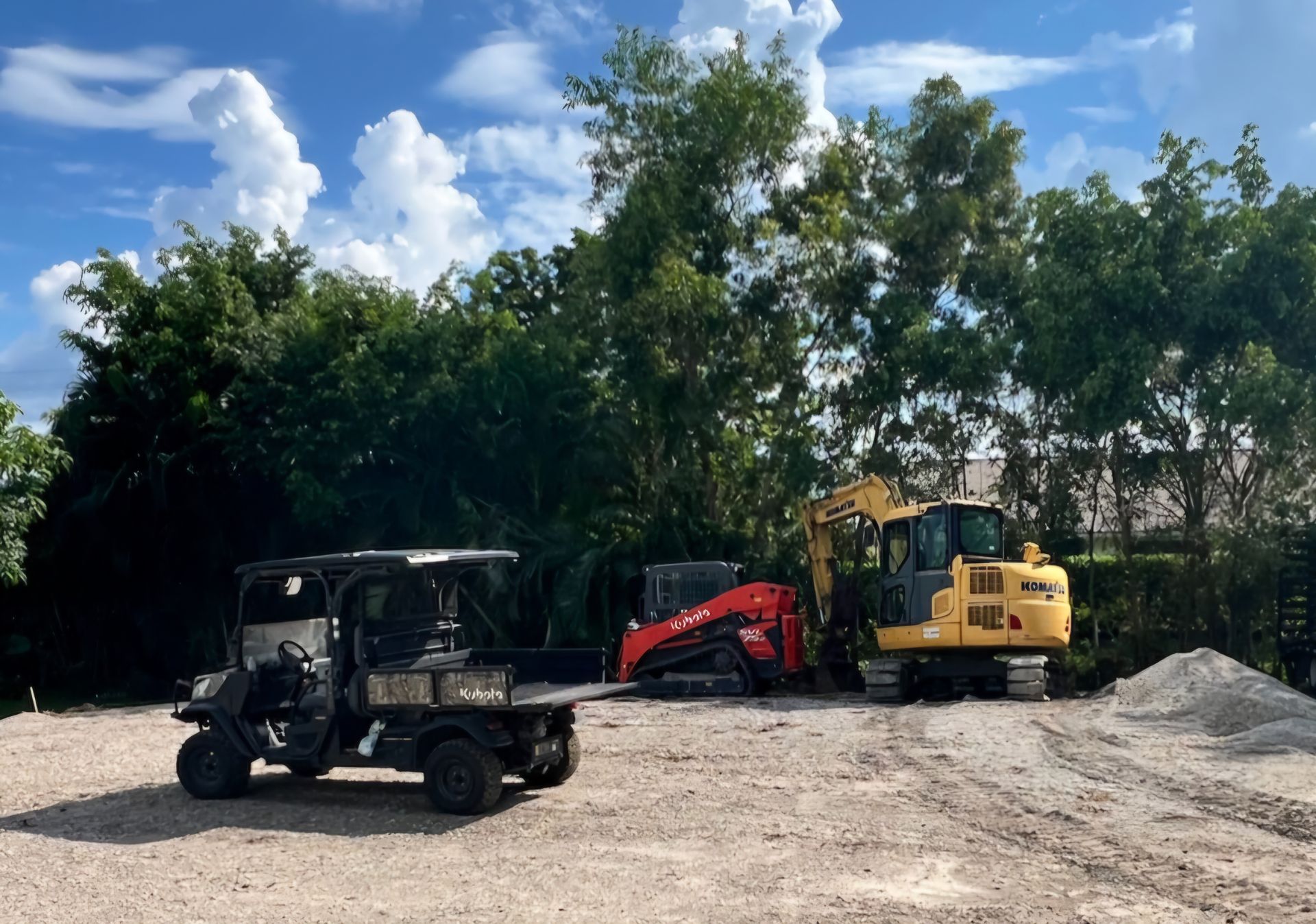 A golf cart is parked next to a bulldozer in a dirt lot.