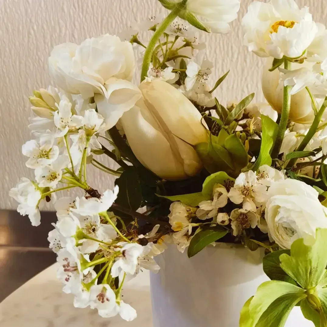 A white vase filled with white flowers and green leaves