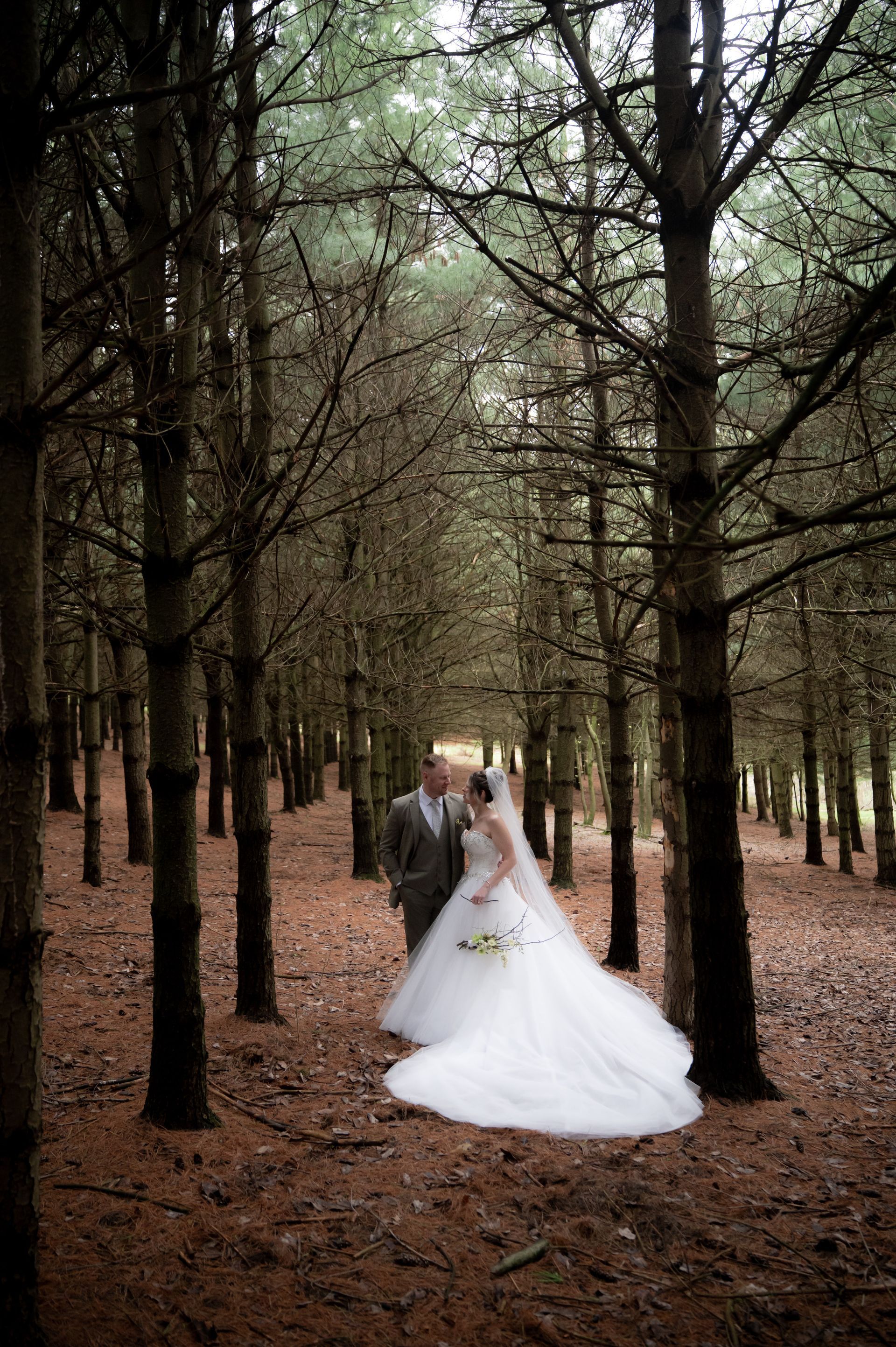 A bride and groom are standing in the middle of a forest.