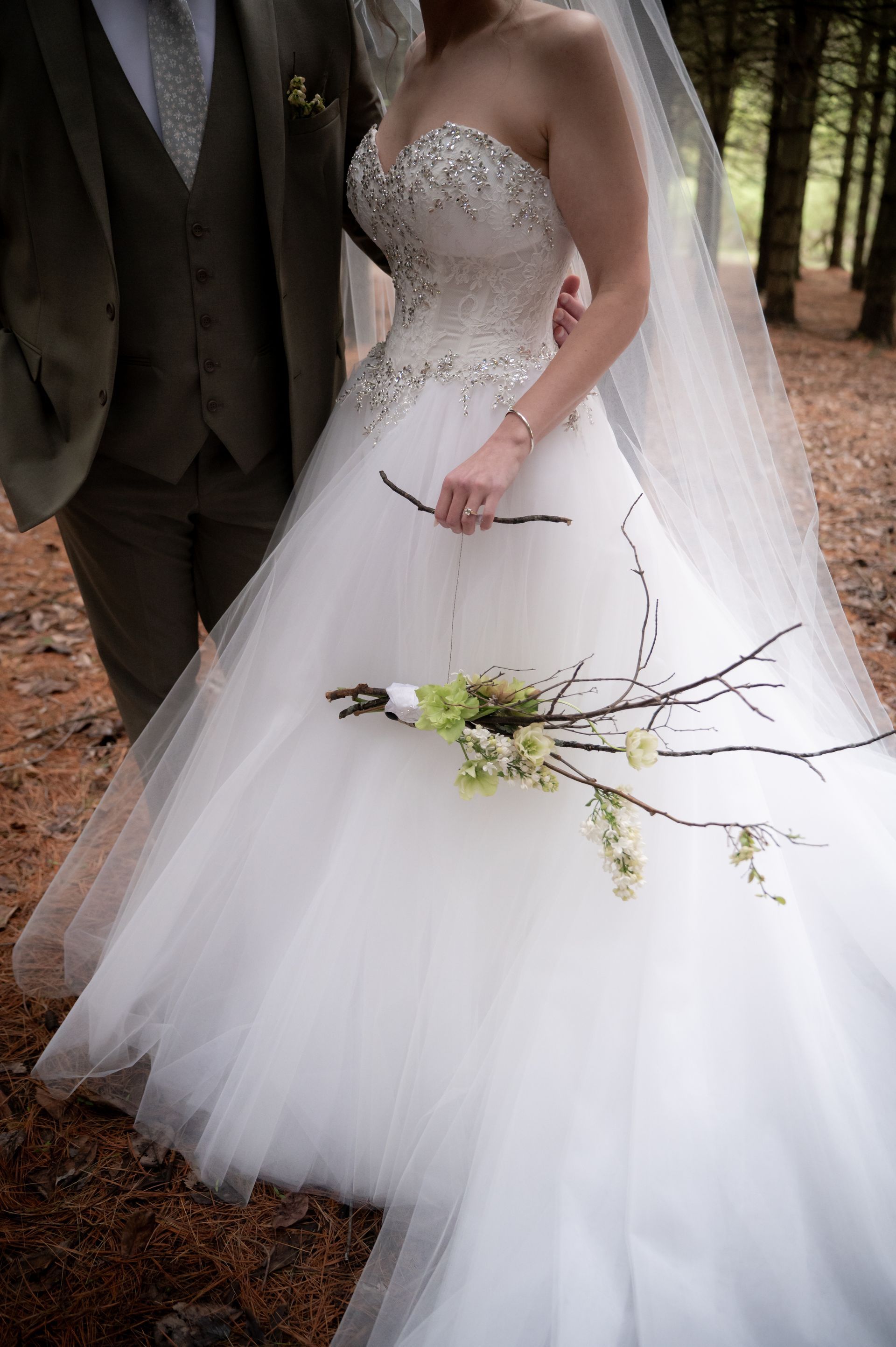 A bride and groom are standing in the woods holding a bouquet of flowers.