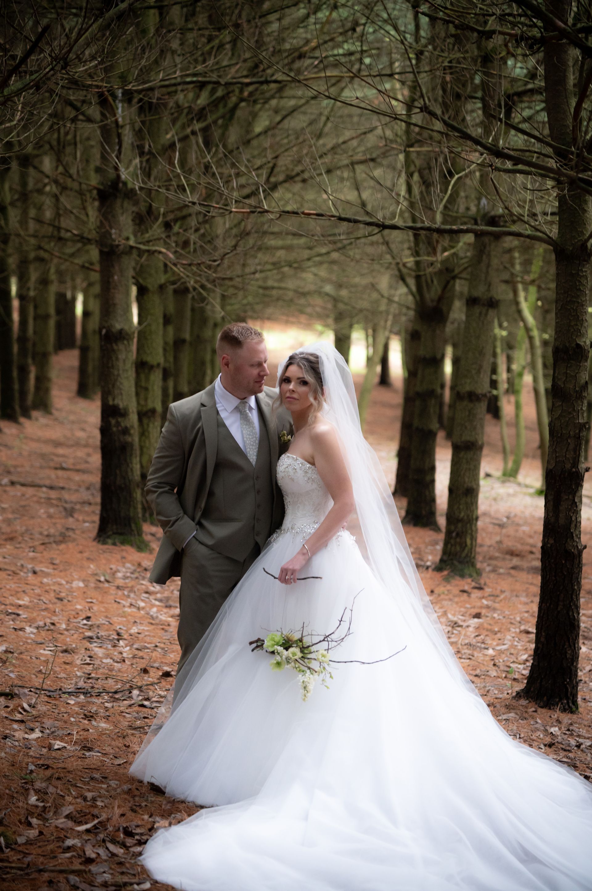 A bride and groom are posing for a picture in the woods.