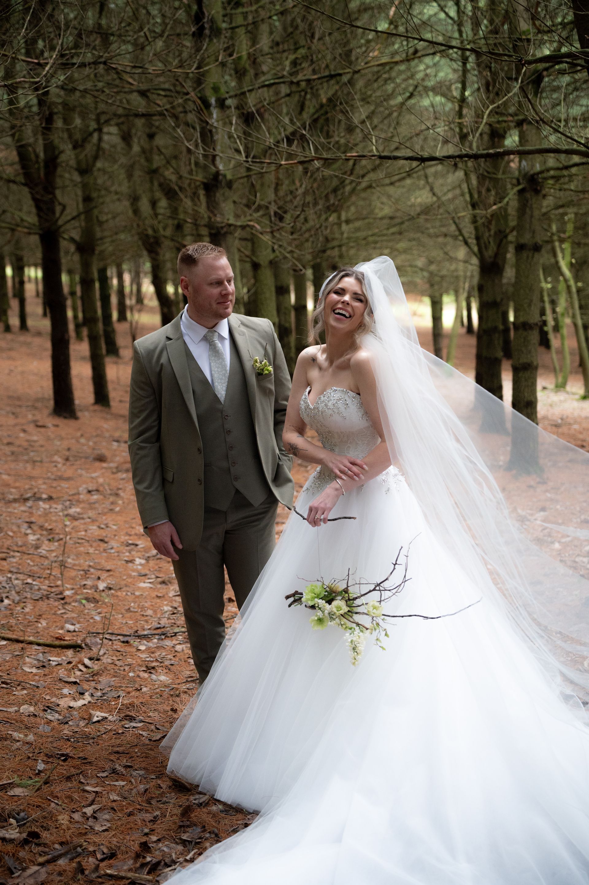 A bride and groom are posing for a picture in the woods.