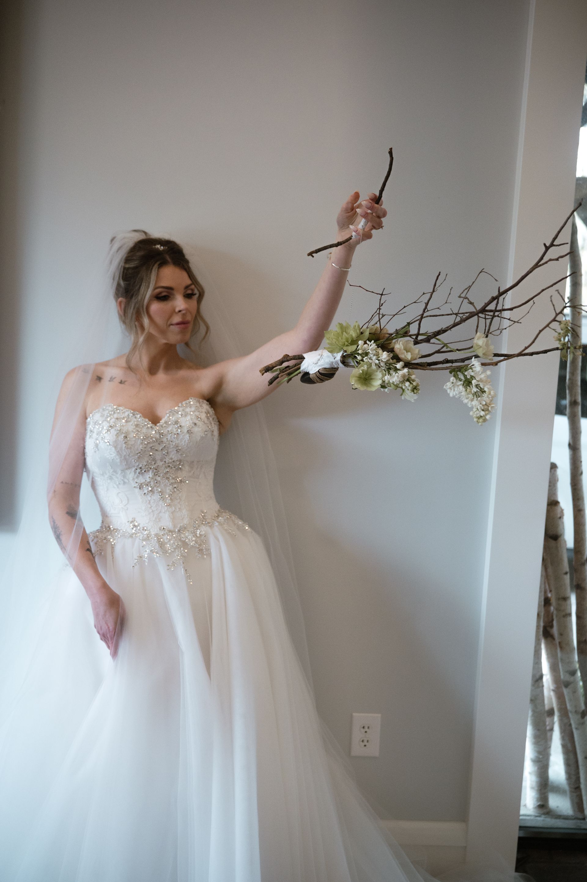 A woman in a wedding dress is standing in front of a mirror holding a branch.