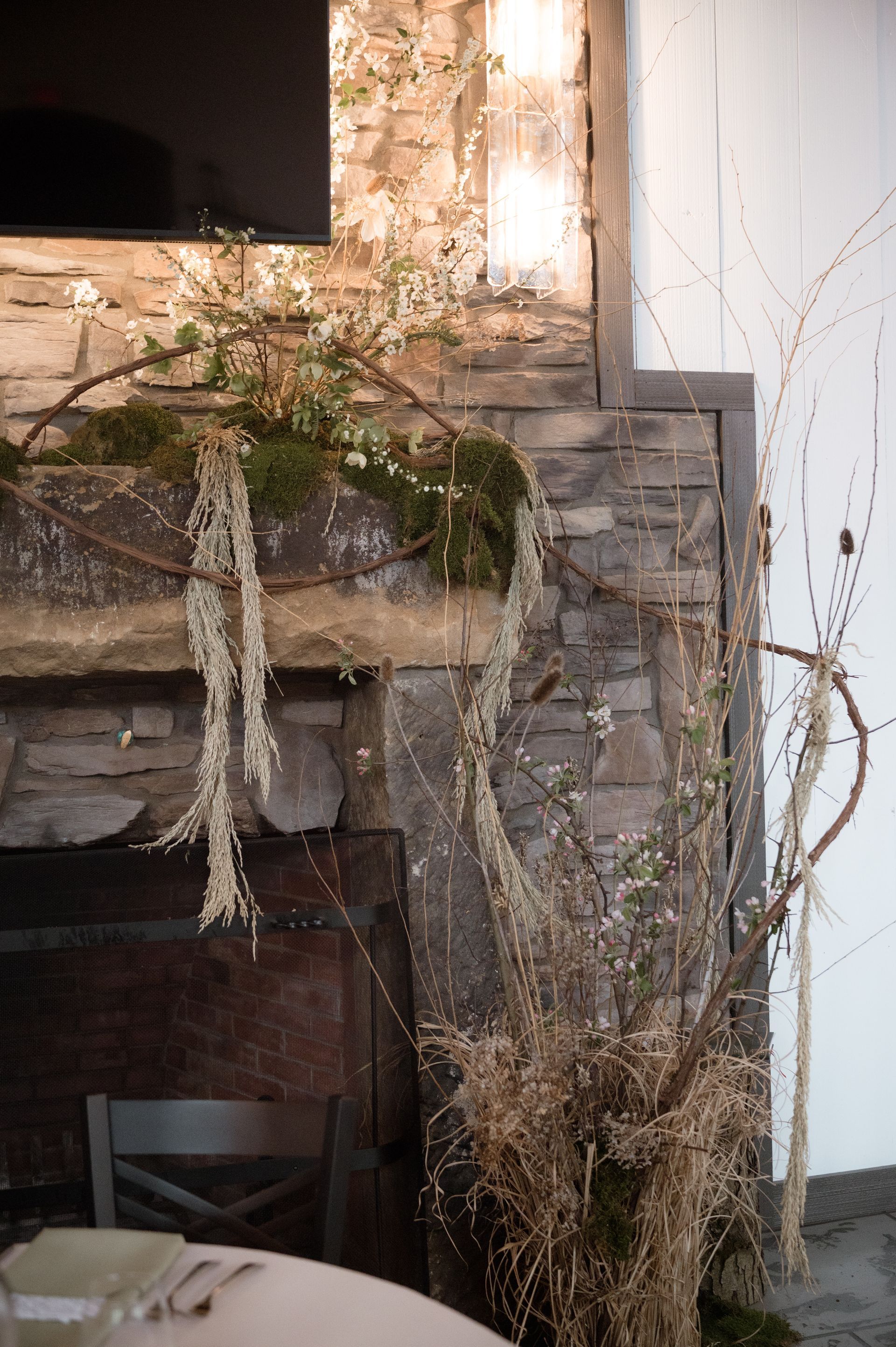 A fireplace with branches and flowers on it and a table in front of it.