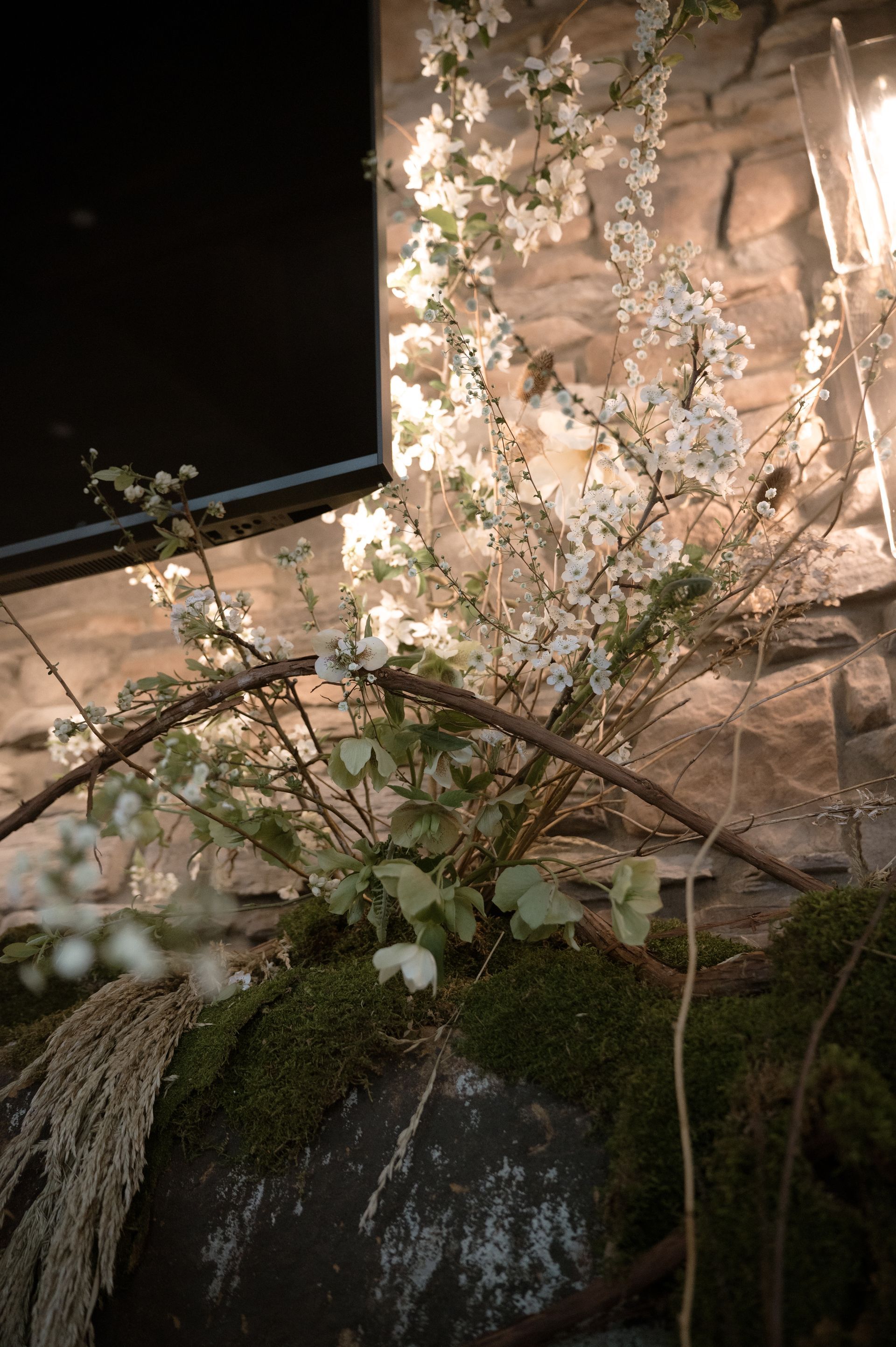 A vase filled with flowers and moss is sitting in front of a stone wall.