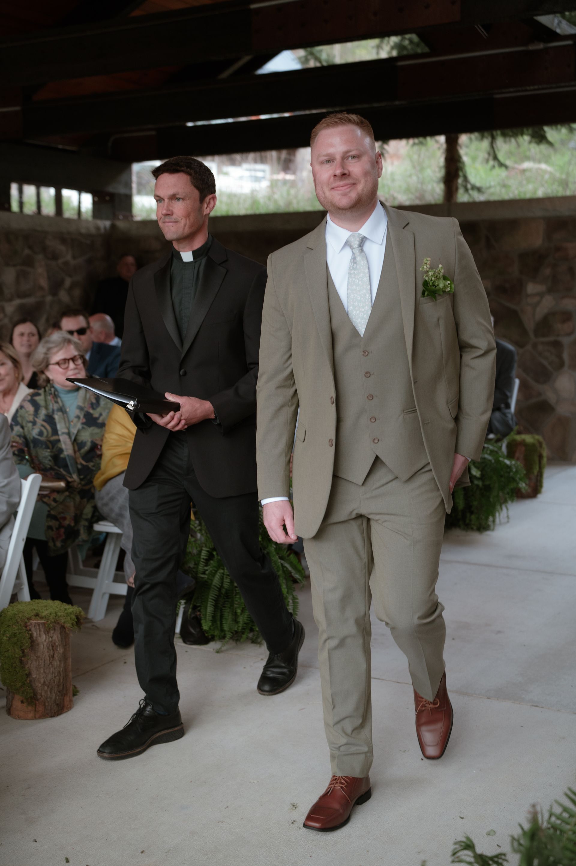 Two men in suits are walking down the aisle at a wedding.