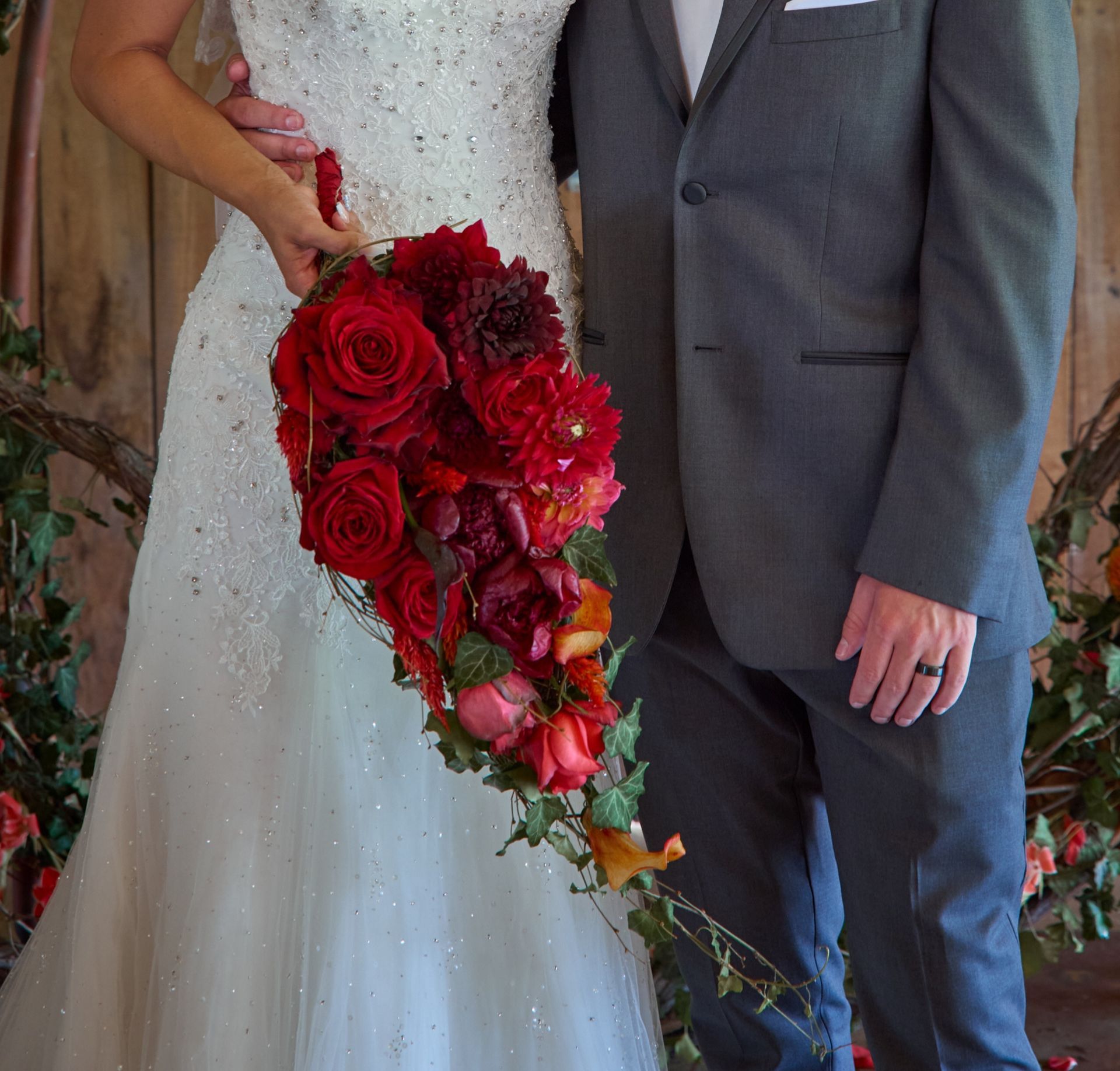A bride and groom pose for a picture while the bride holds a bouquet of red roses