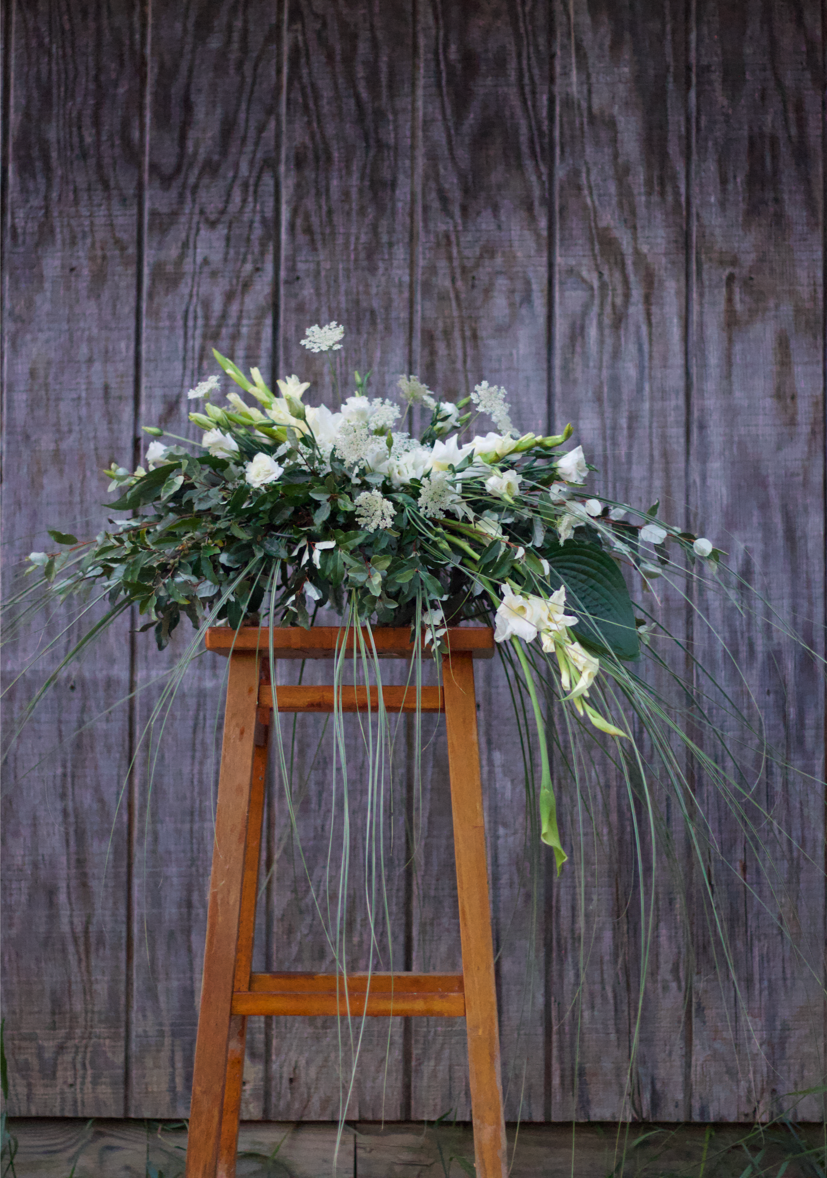 A wooden stool with flowers on it in front of a wooden wall.