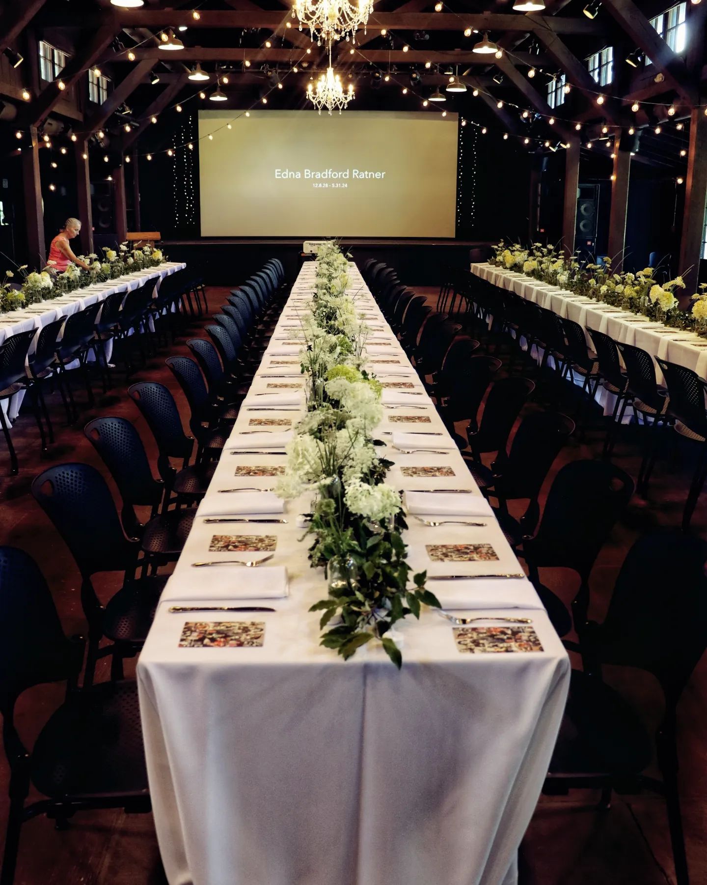 A long table with flowers on it in front of a large screen