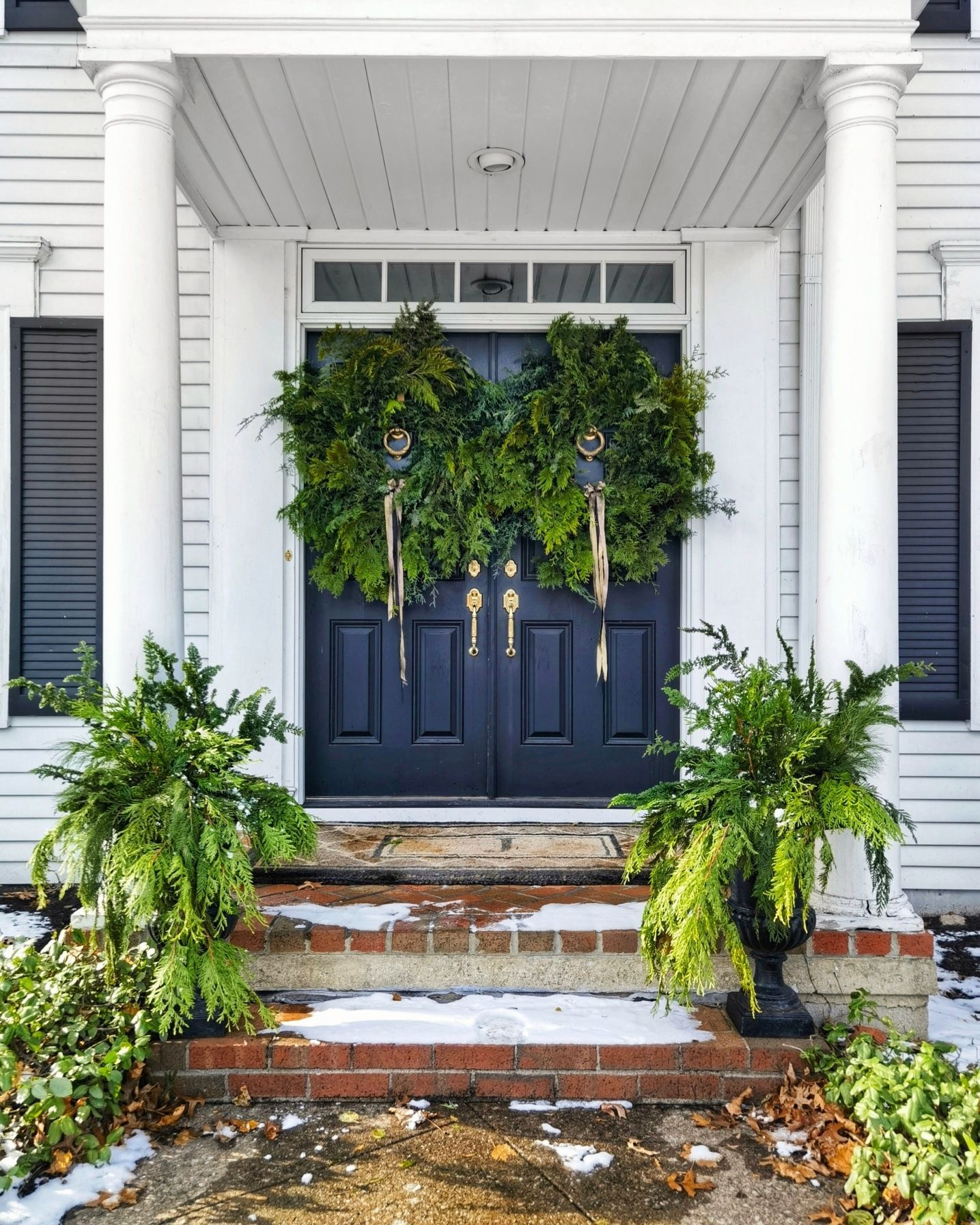The front door of a house is decorated with wreaths and ferns