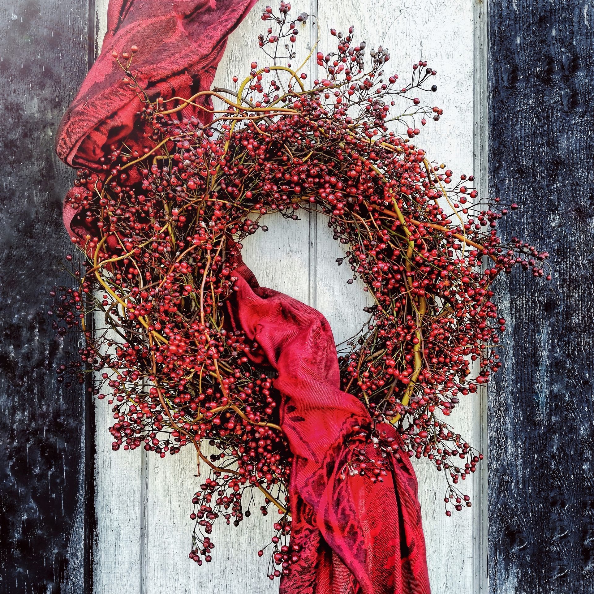 A wreath with red berries and a red scarf hanging on a door