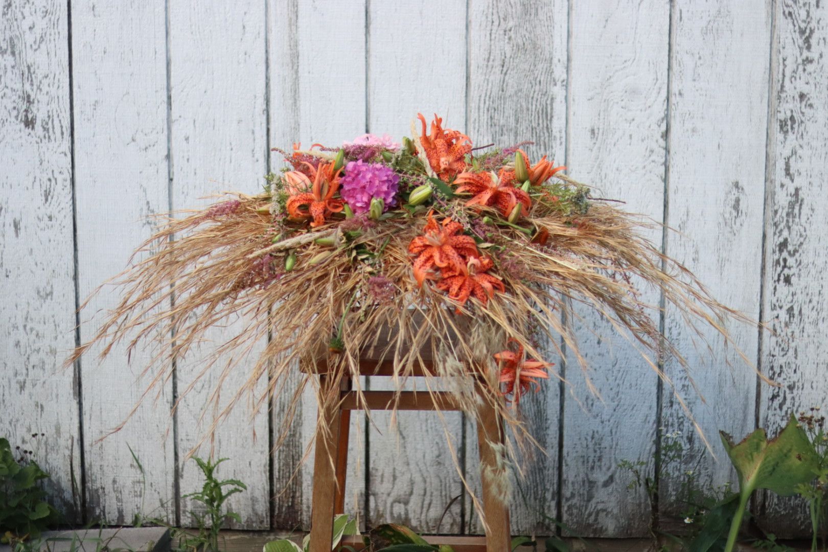 A wooden stool with flowers on it in front of a wooden wall.