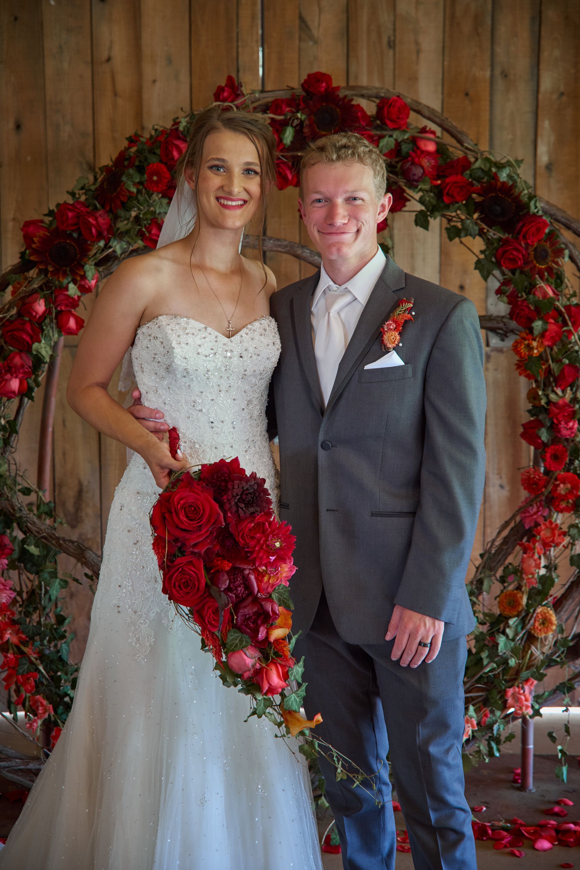 A bride and groom are posing for a picture in front of a floral arch.