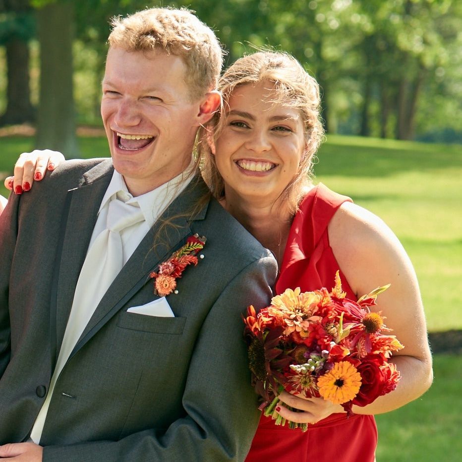 A woman in a red dress holds a bouquet of flowers next to a man in a suit
