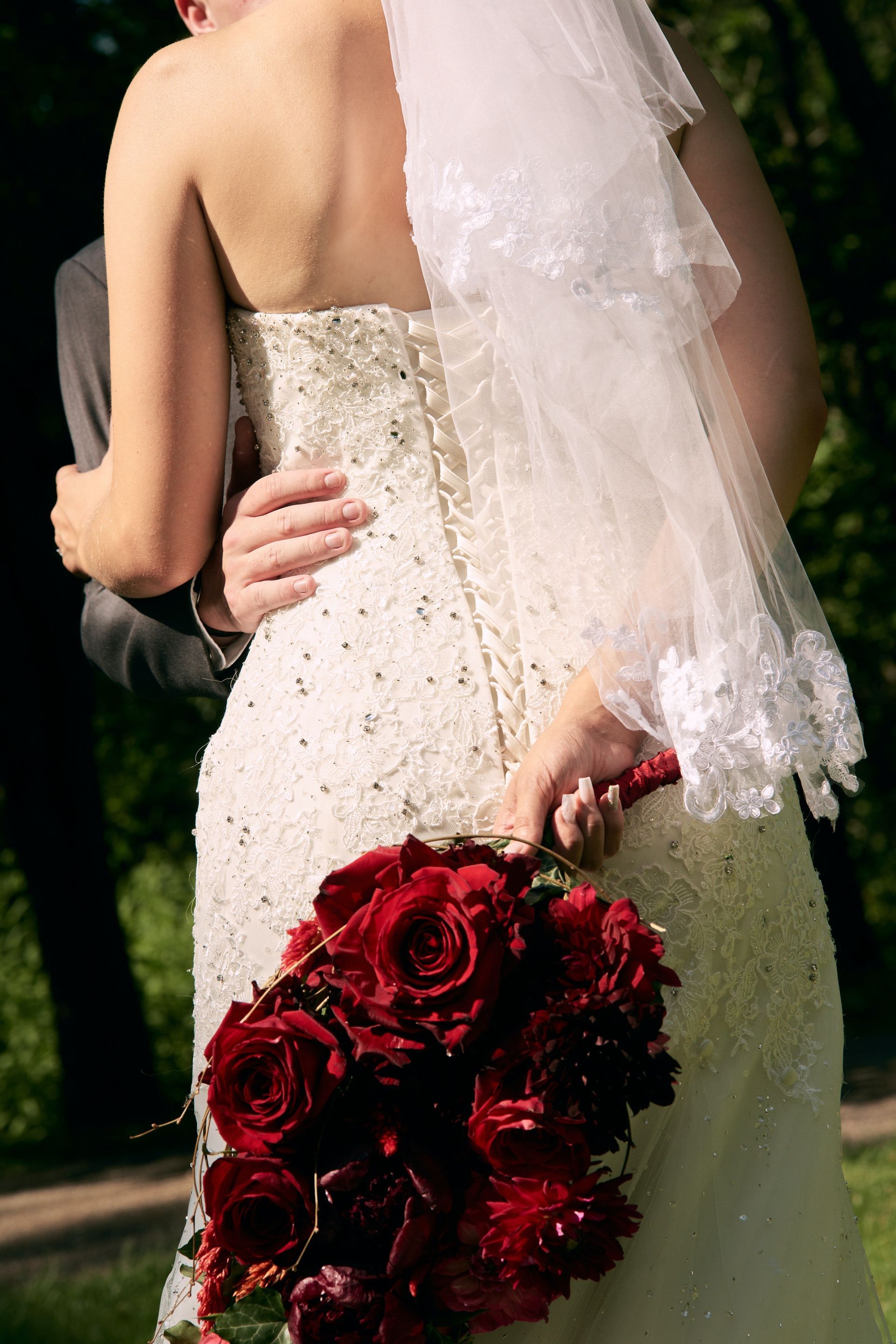 The bride is holding a bouquet of red roses behind her back