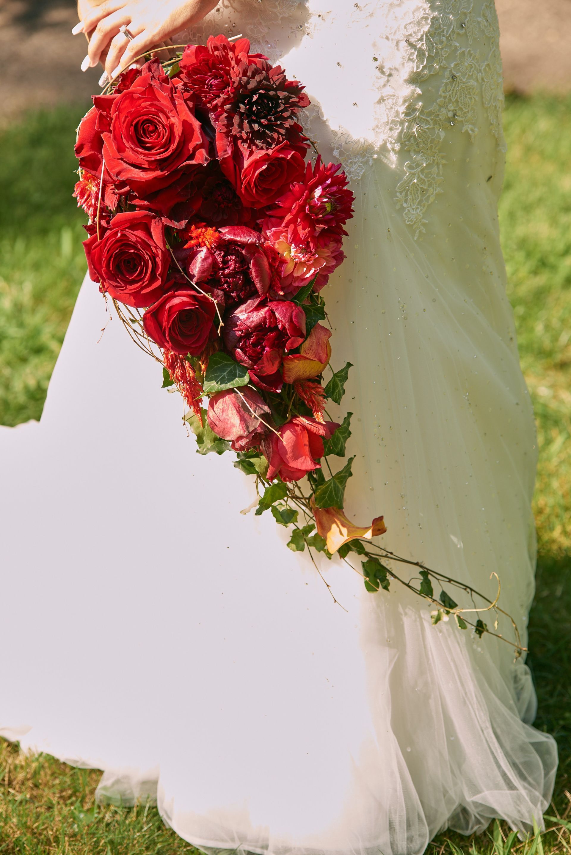 A bride in a white dress is holding a bouquet of red flowers.