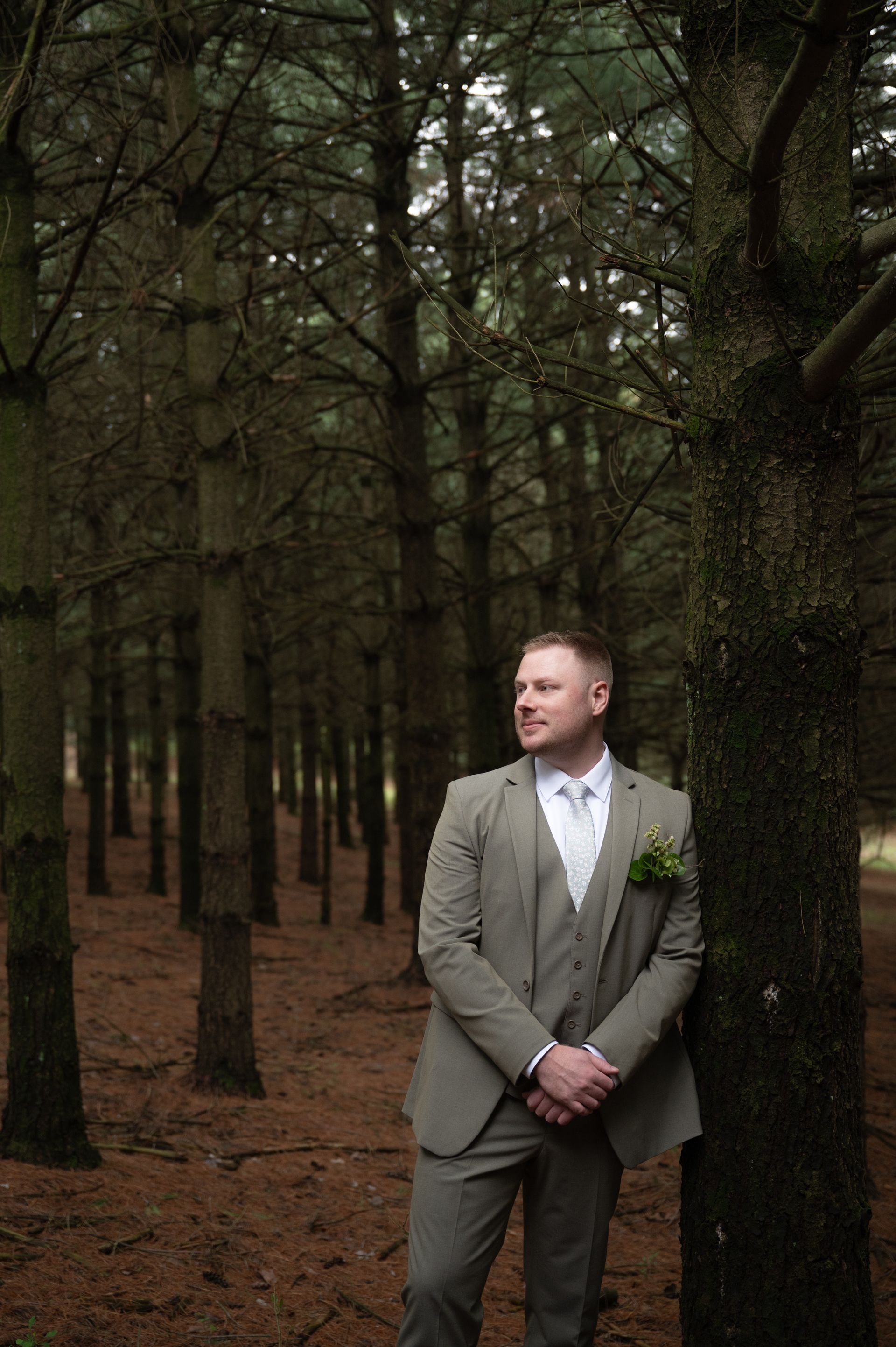 A man in a suit is leaning against a tree in the woods.