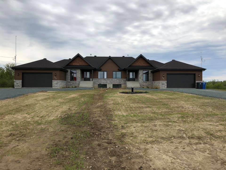 Une grande maison avec deux garages est située au sommet d'un champ verdoyant.