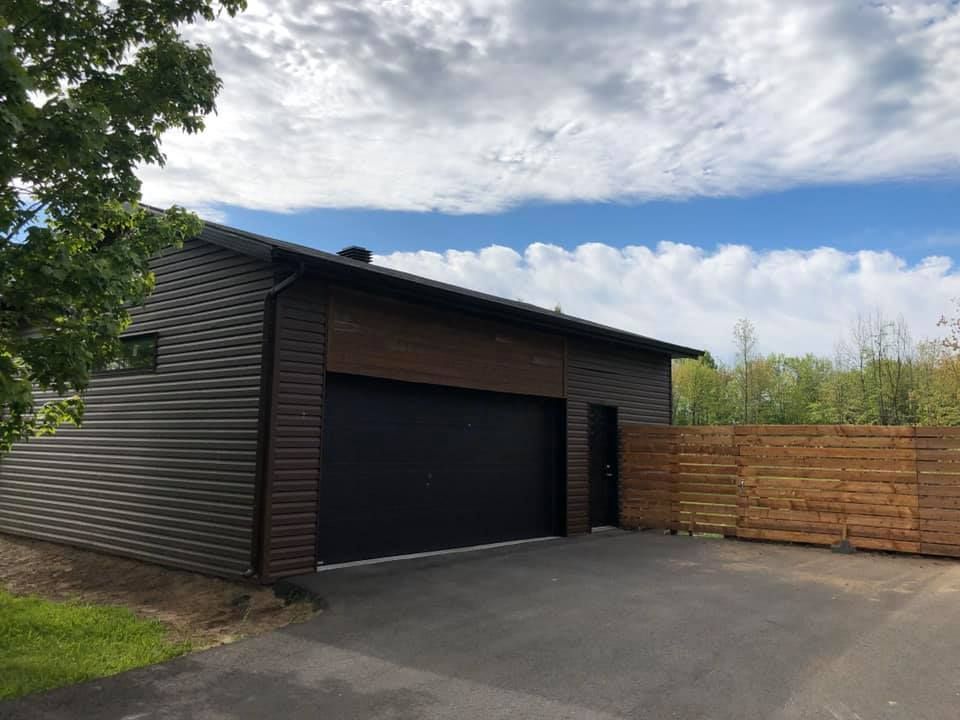 Un garage avec une porte noire et une clôture en bois devant.