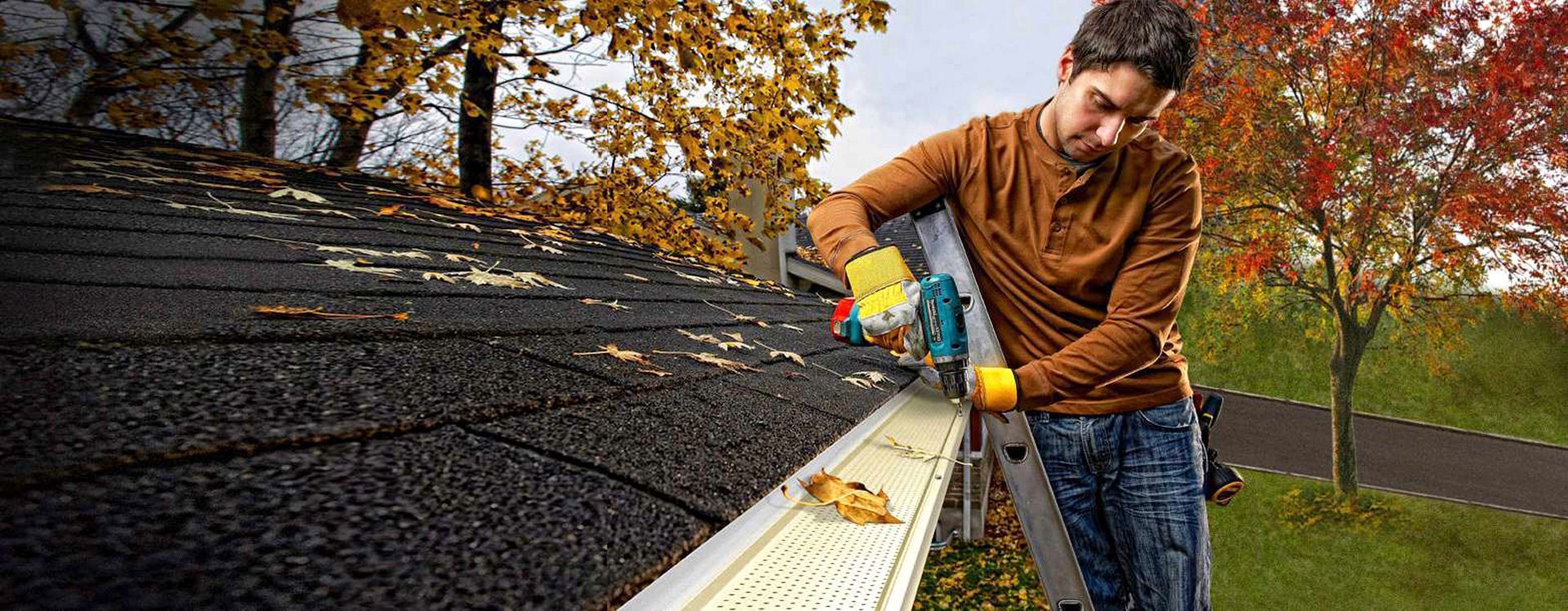 Un homme nettoie une gouttière sur un toit avec une échelle.