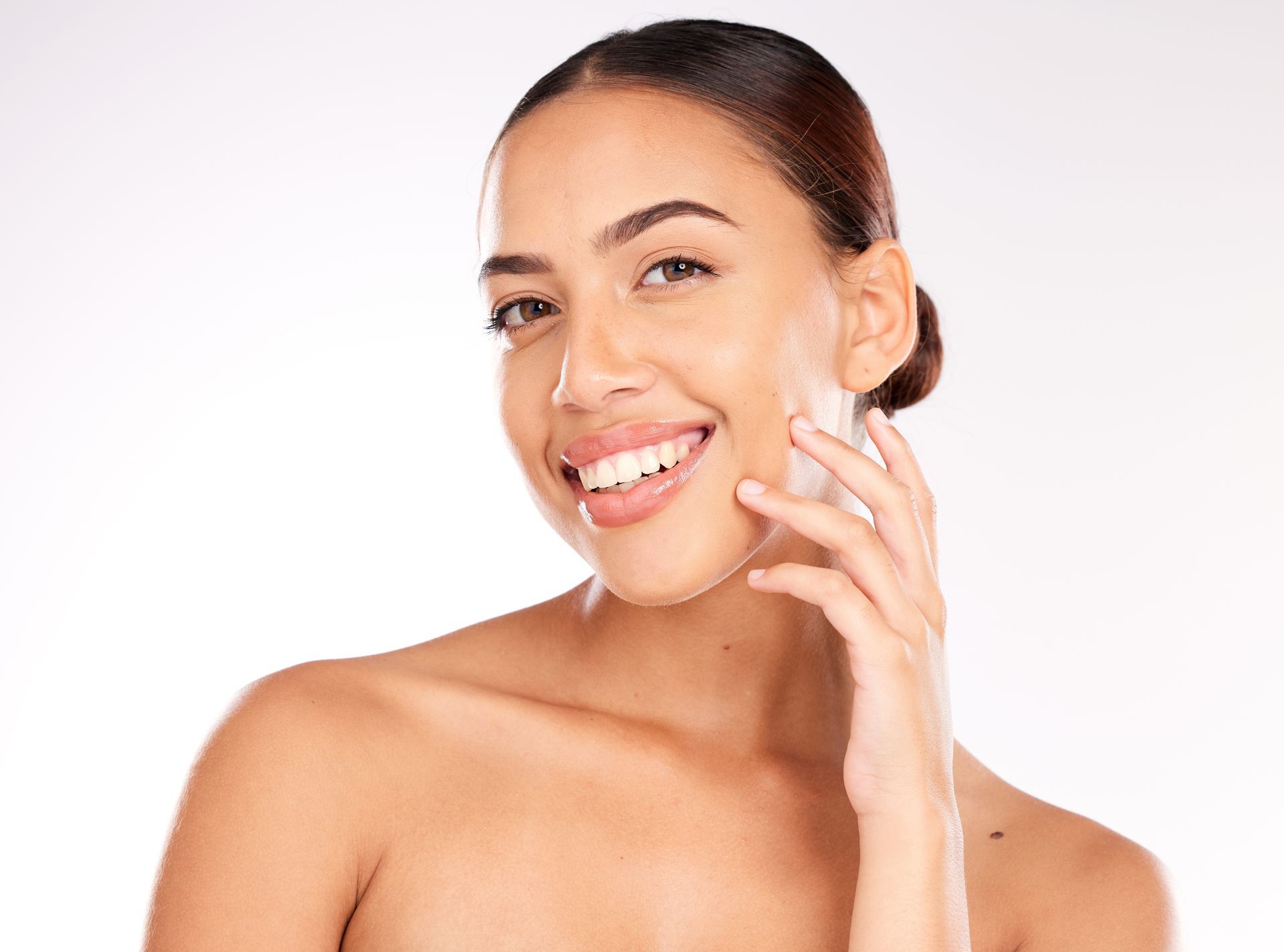 Woman with smooth skin smiling, touching her cheek with skincare product on a white background.