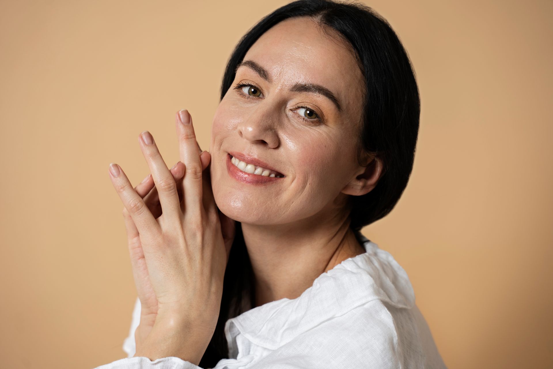 A woman is smiling and touching her face with her hands.
