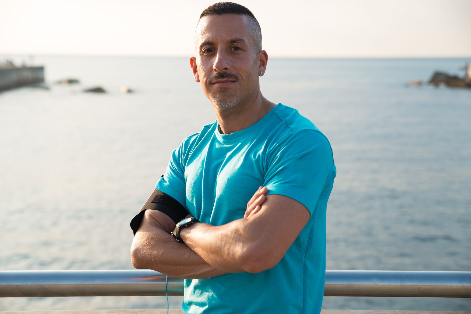 A man in a blue shirt is standing on a pier with his arms crossed.