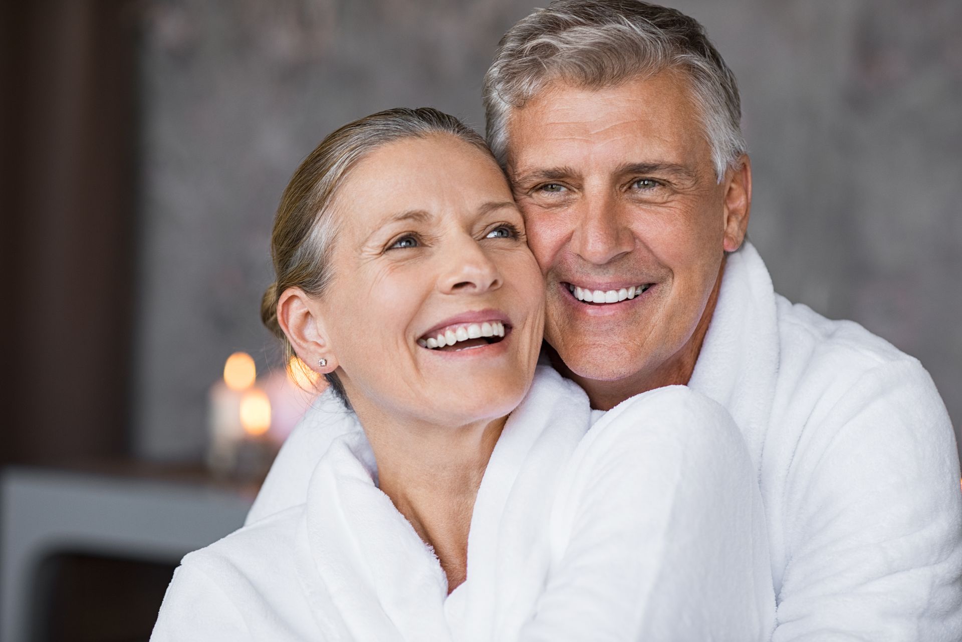 Smiling senior couple in white robes embracing at a spa, looking content.