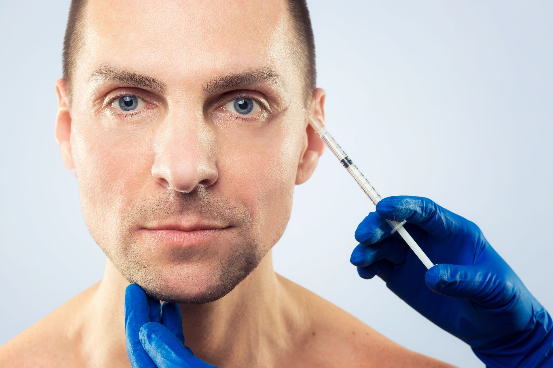 Man receiving a facial injection with a syringe in a clinical setting.