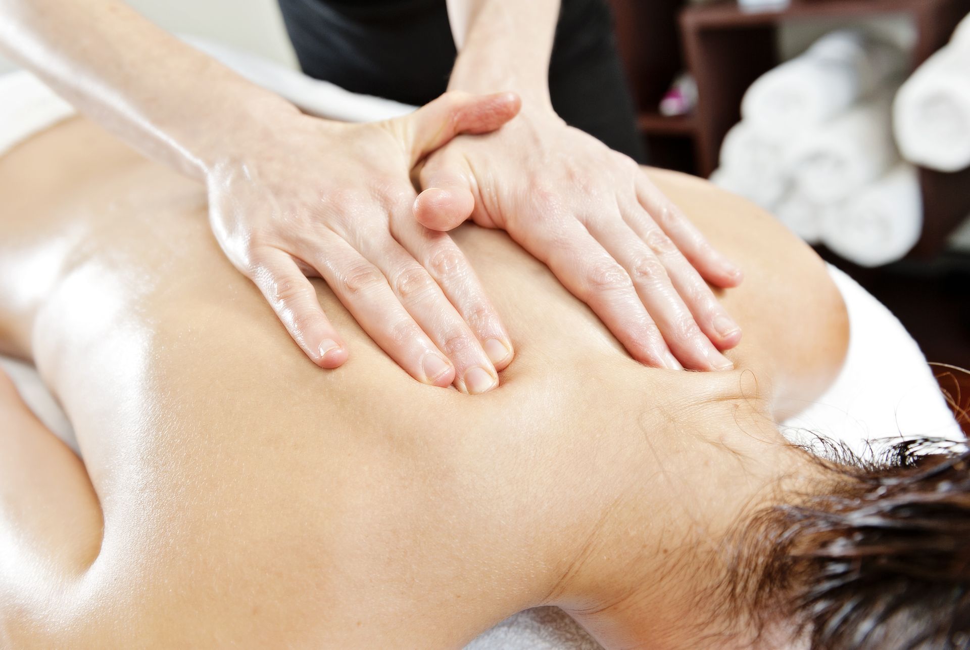 Person receiving a back massage, hands of masseuse applying pressure.