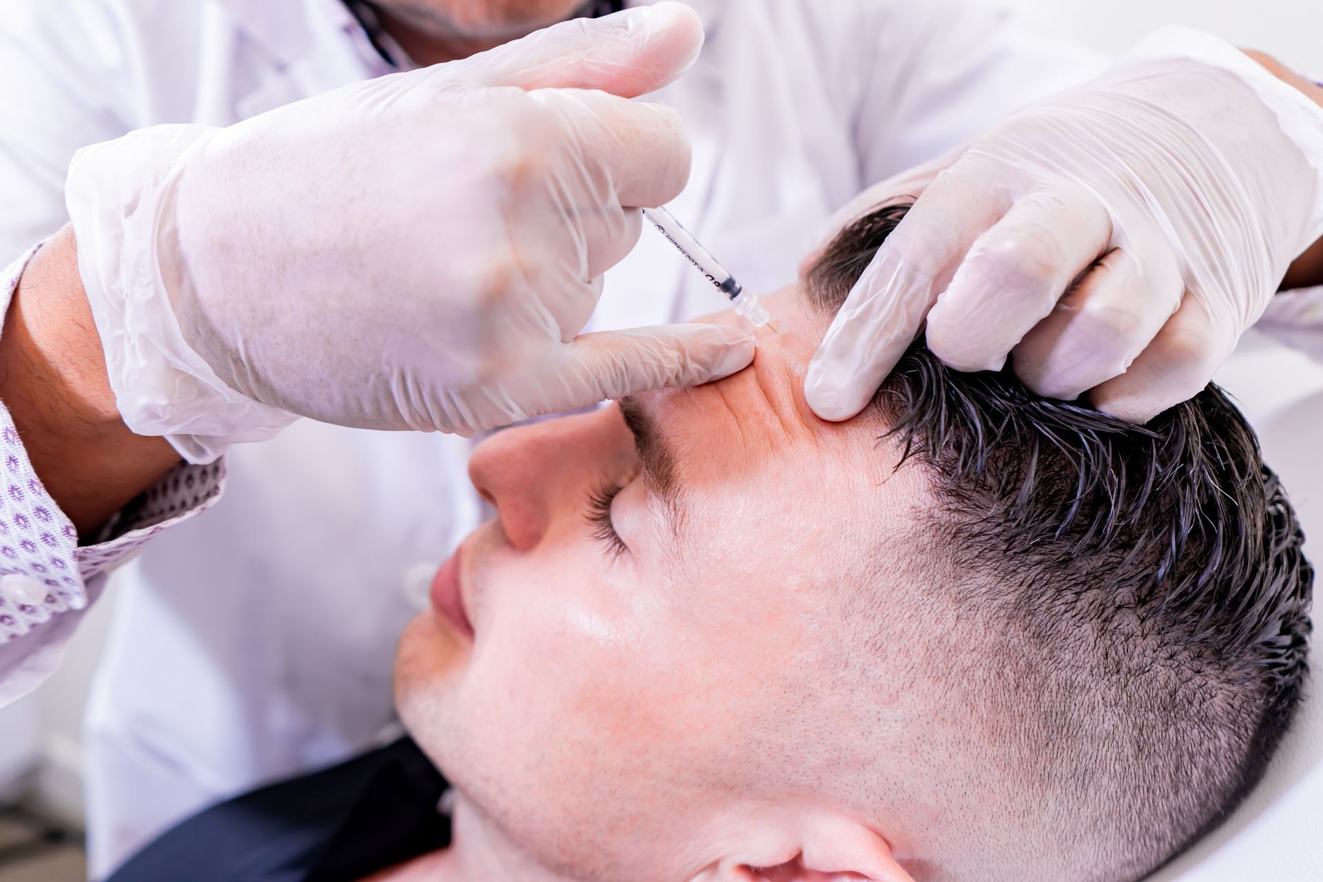 Man receiving a facial injection on his forehead from a gloved professional.