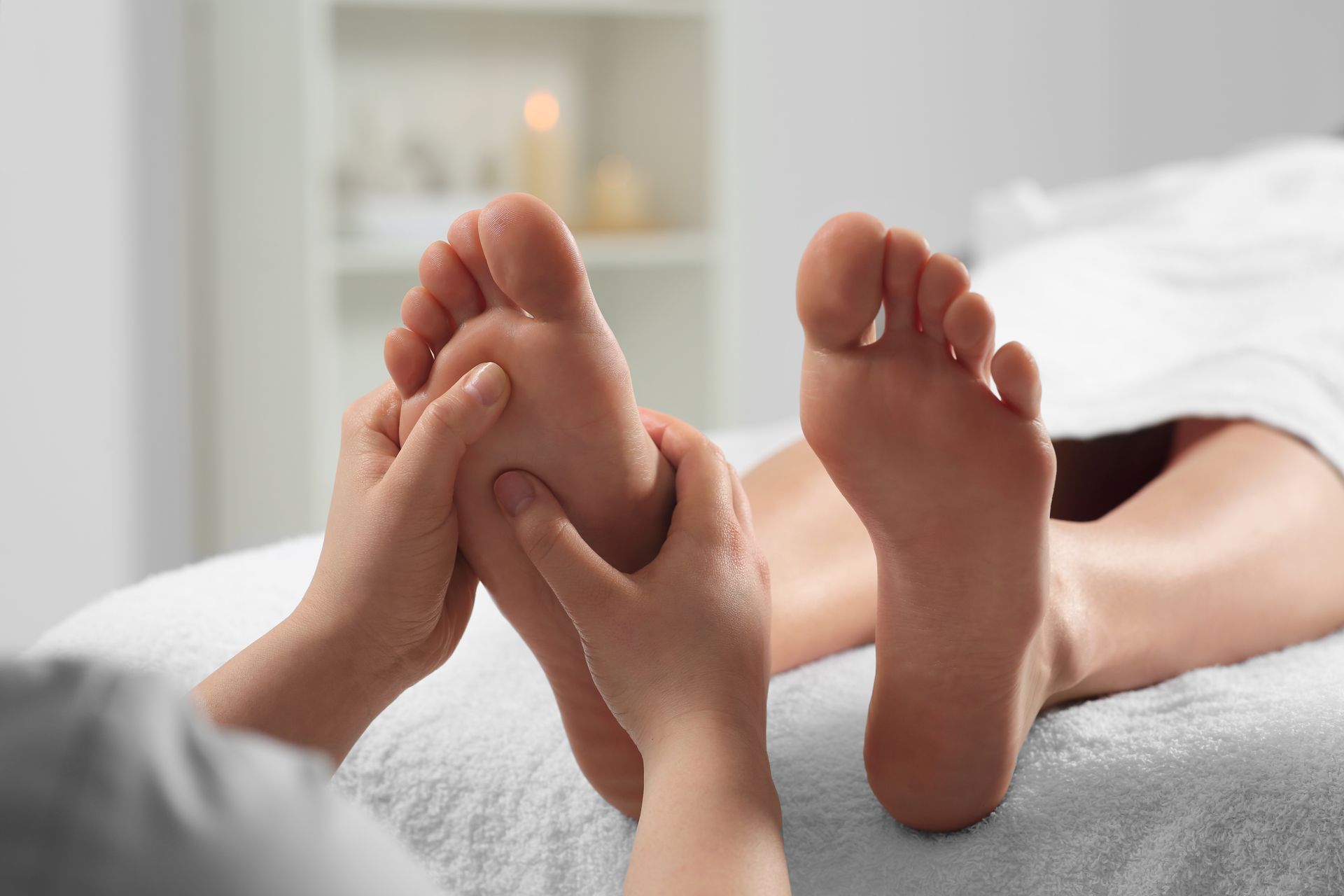 Person receiving foot massage on a white bed. Hands gently massage the sole.