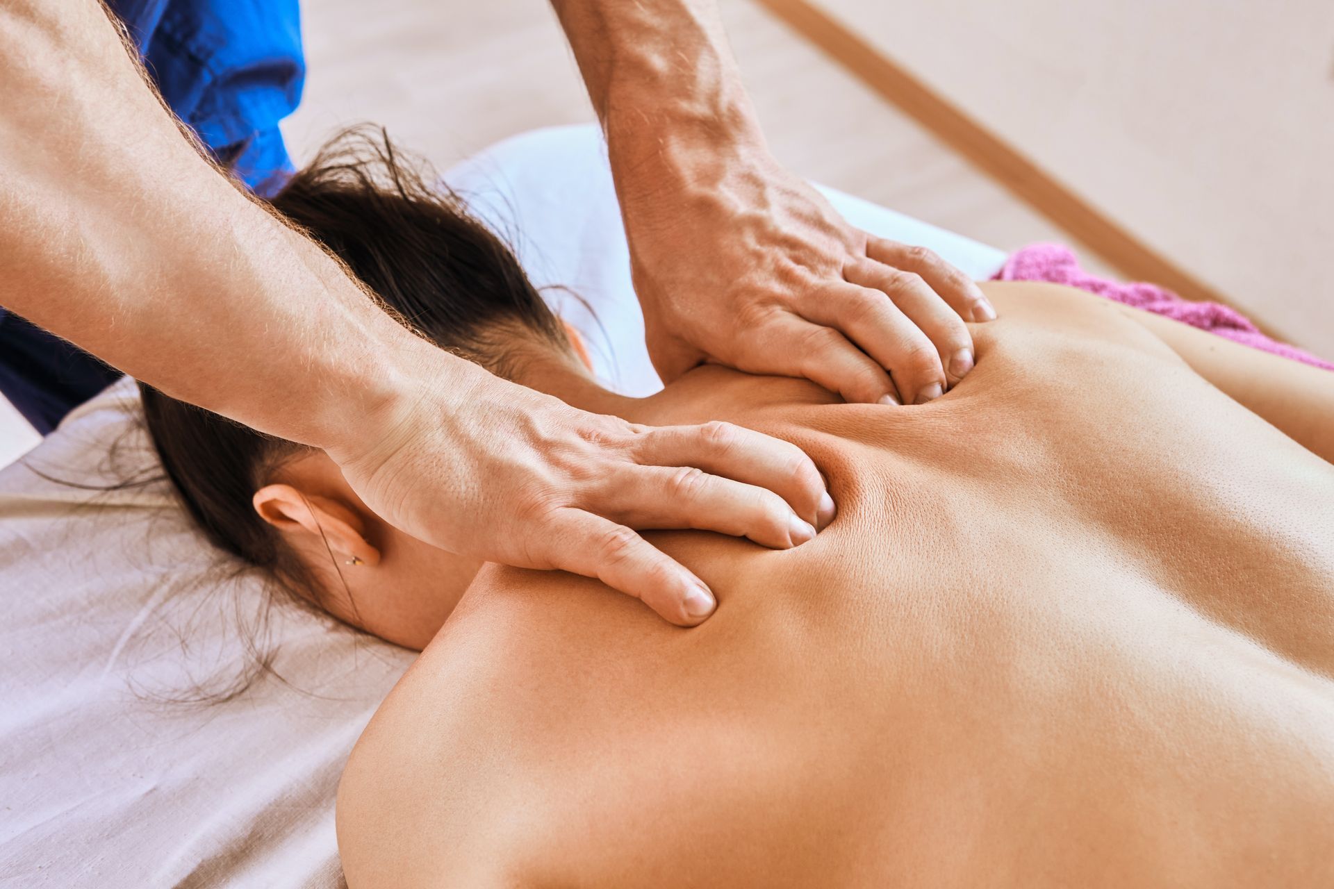 A person receiving a back massage from a therapist in a light-filled room.