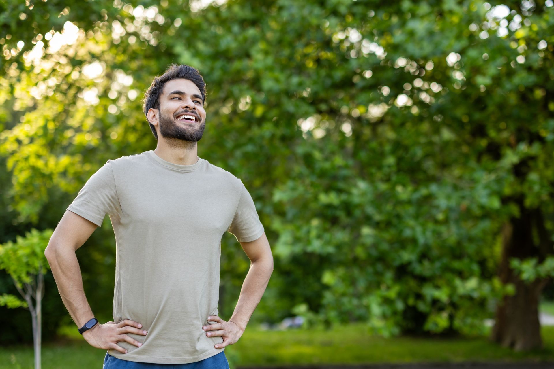 A man with his hands on his hips is standing in a park.
